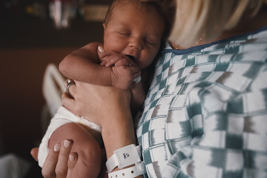 Newborn sleeping while being cradled against a parent’s chest in a hospital gown