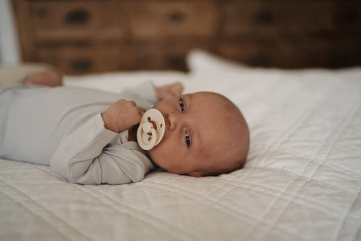 Baby lying on a bed with a pacifier in mouth, looking towards the camera
