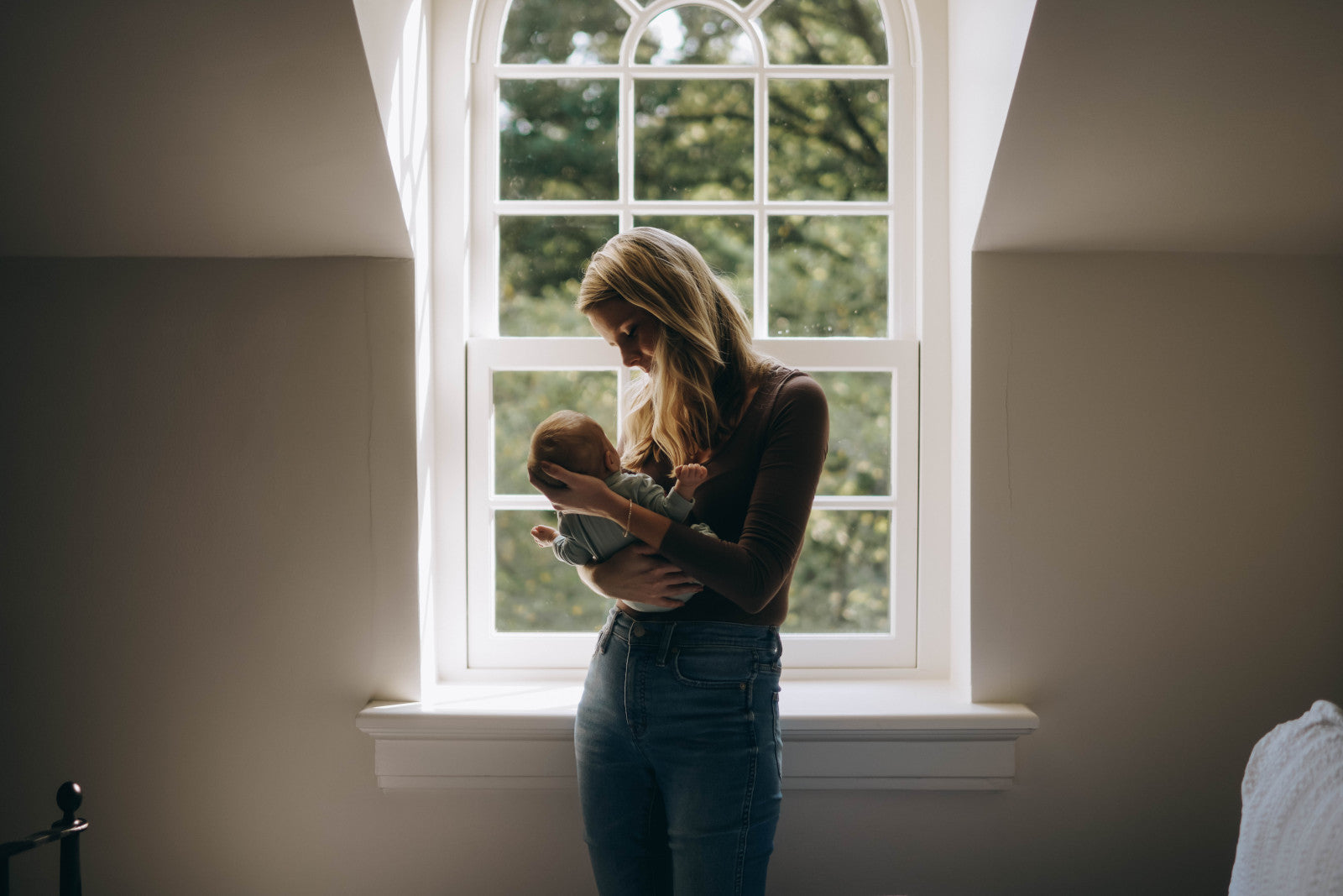 Mother cradling a newborn in front of a window with soft natural light