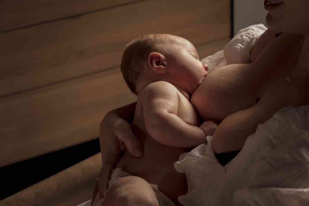 Mother breastfeeding a newborn, cradling the baby against her chest in warm low light