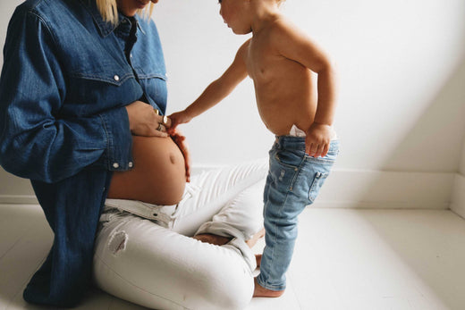 Pregnant woman sitting on the floor with a toddler touching her baby bump.