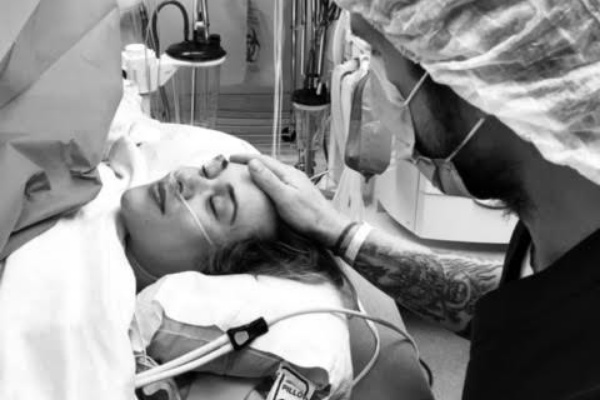 Woman lying in a hospital bed during labor with oxygen tubing as her partner holds her head in a delivery room