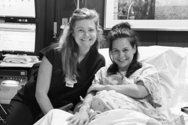 Susanna Stanbury smiling beside a woman in a hospital bed in a clinical room