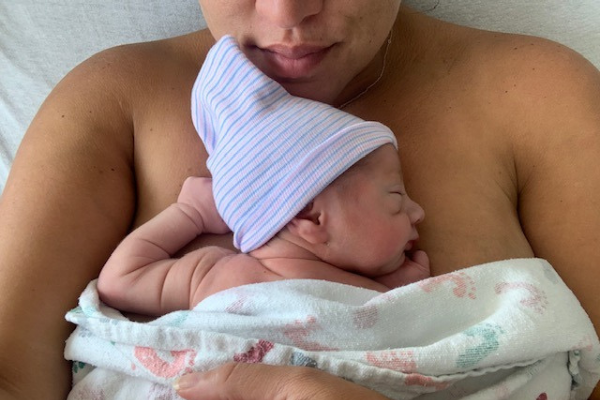 Person holding a newborn baby for skin-to-skin contact, baby wrapped in hospital blanket and wearing a striped cap