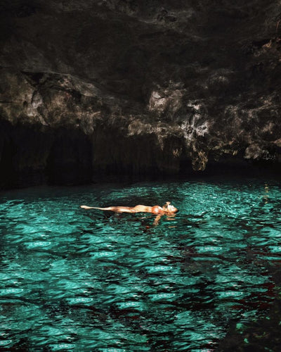 Person floating on clear turquoise water inside a dark cave with rocky ceiling