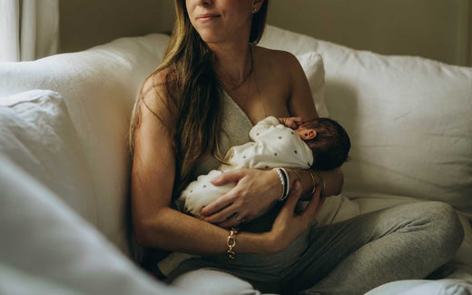 Woman sitting on a couch holding a newborn baby wrapped in a white blanket with black dots.