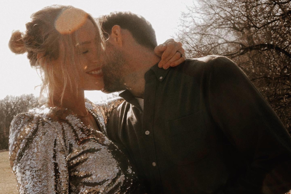 Couple embracing and kissing outdoors in warm backlight, woman smiling in a sequined top