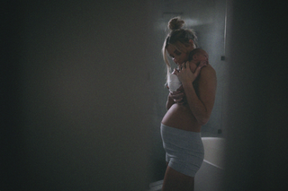 A woman holding a newborn baby close to her chest in a dimly lit room, conveying a tender moment of bonding.