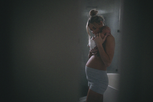 A woman holding a newborn baby close to her chest in a dimly lit room, conveying a tender moment of bonding.