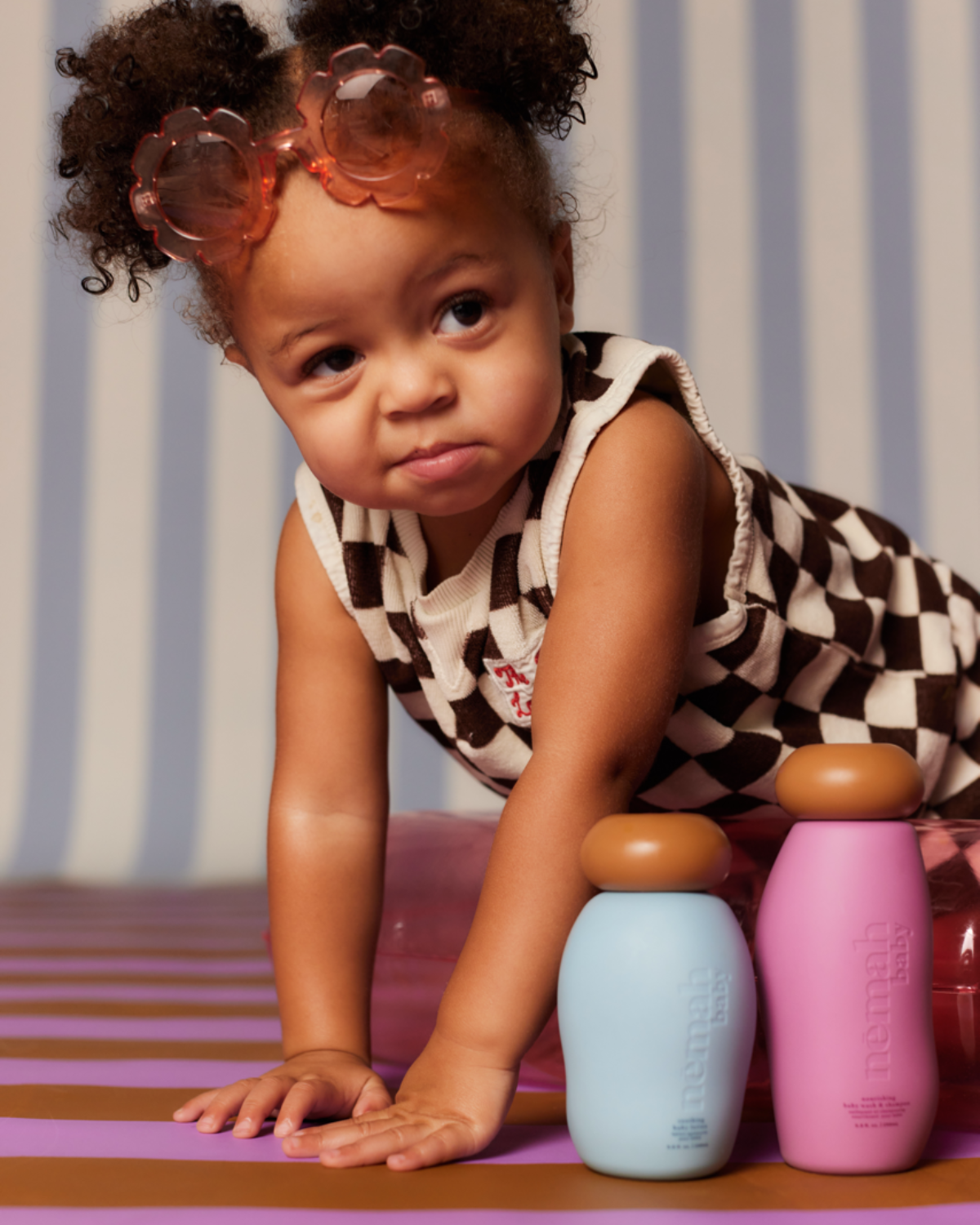 small child with curly hair is crawling in between two colorful bottles 