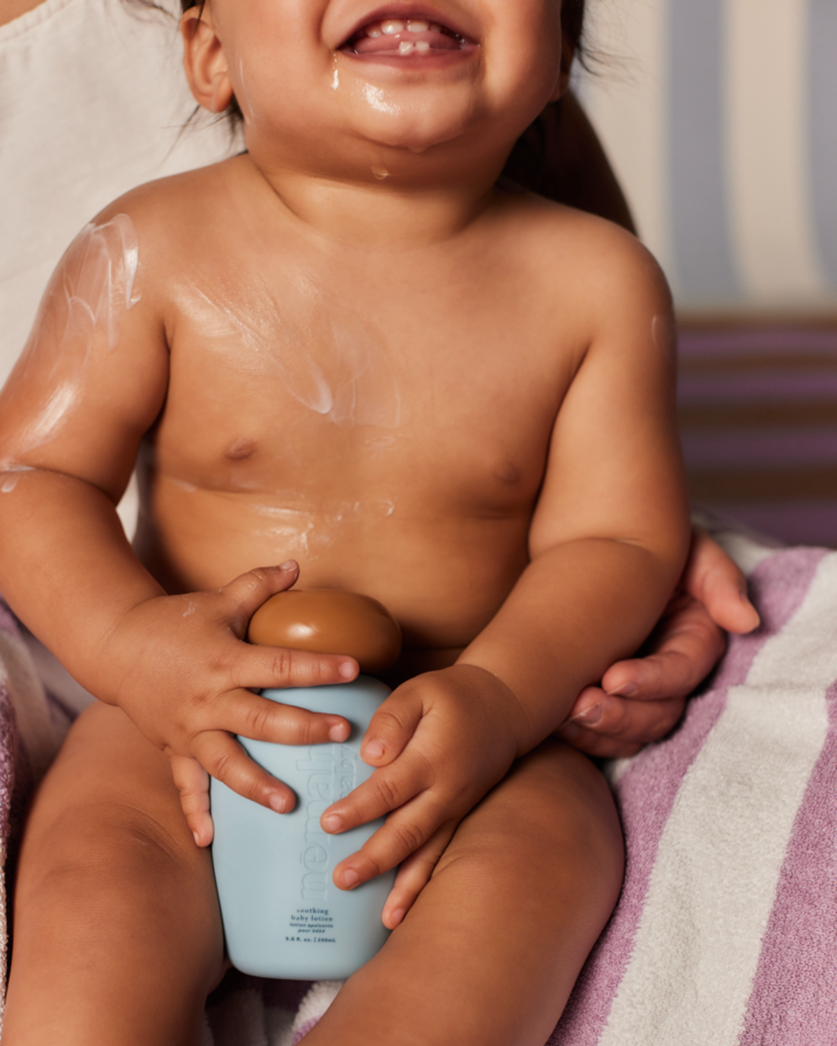 Baby holding a blue bottle with lotion applied on skin