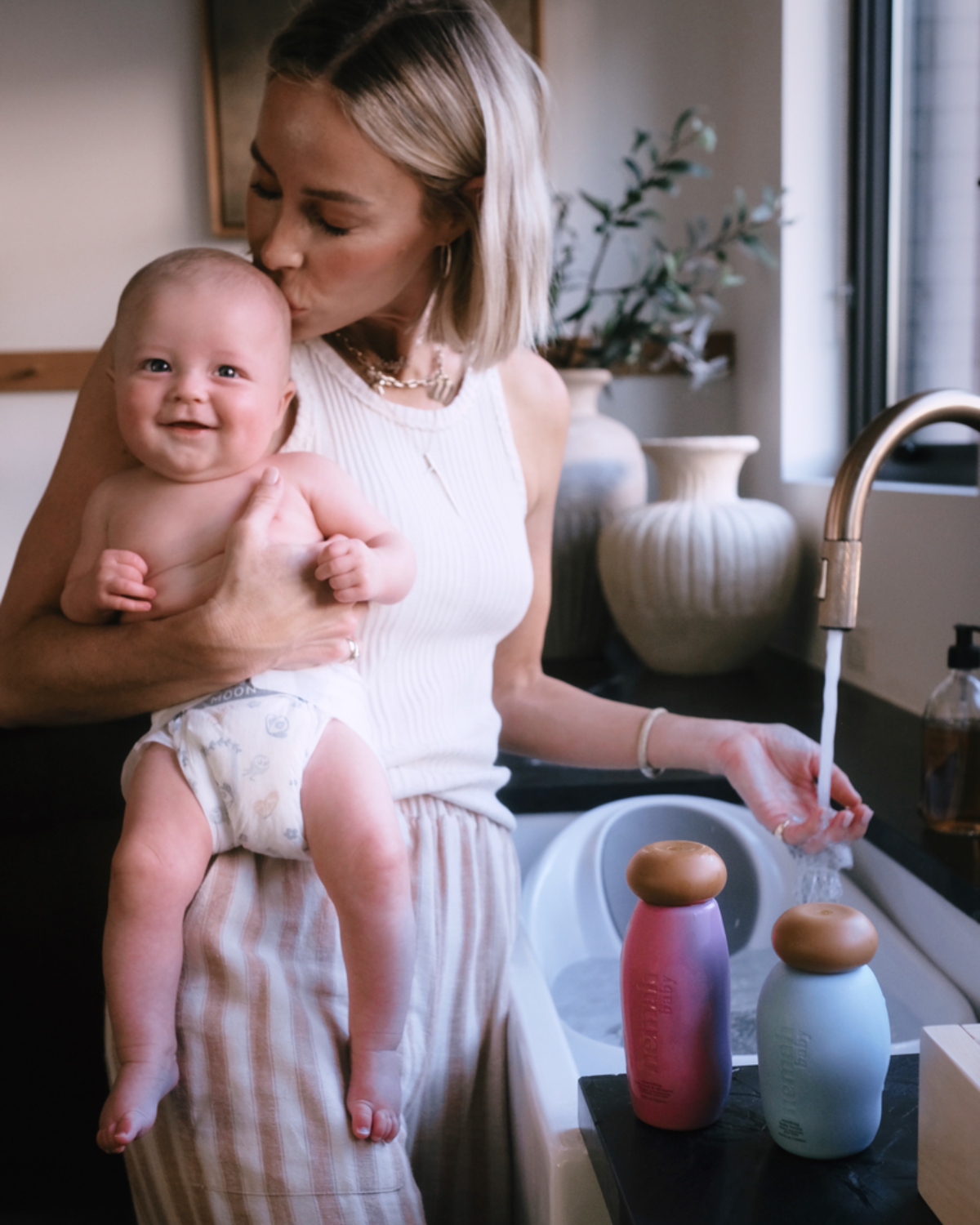 Woman holding baby next to sink with two bottles