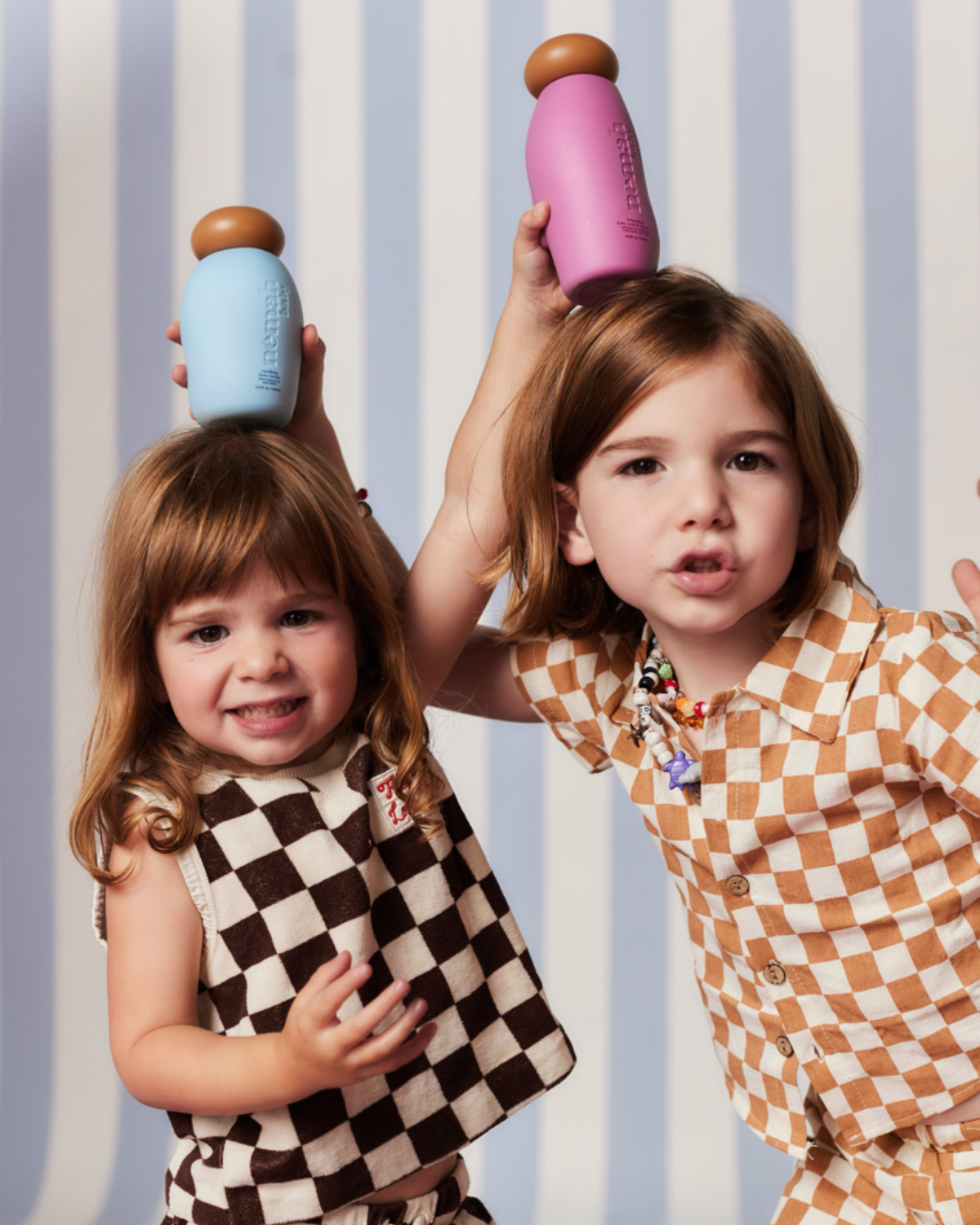 Two children holding colorful bottles on their heads, smiling.