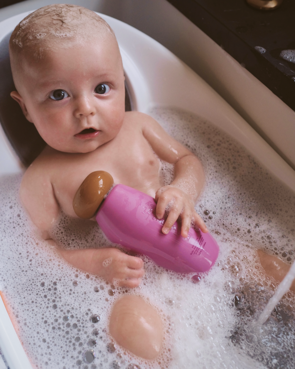 Baby in a bathtub holding a pink bottle