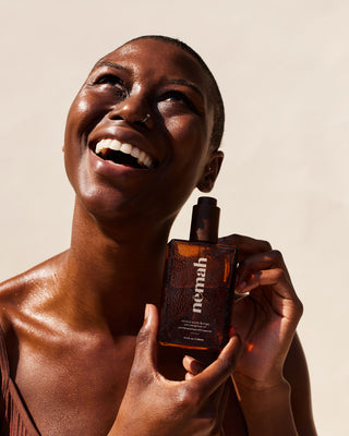 Smiling woman holding amber pump bottle labeled 'nemah' (stretch mark therapy body oil)