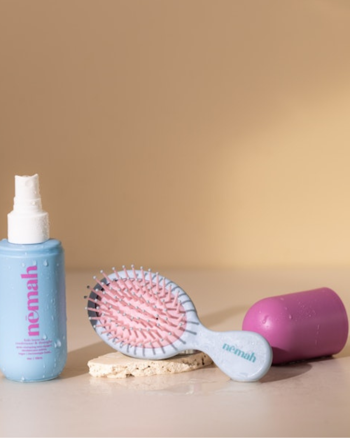 Hair care products including a spray bottle, brush, and container on a surface.