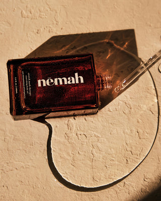 Amber glass dropper bottle labeled nemah lying on textured surface, spilled oil forming a curved line with dropper nearby.
