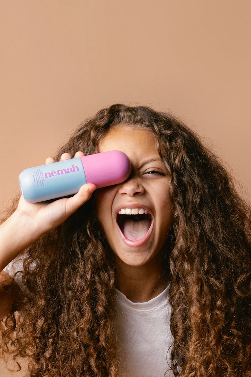 a girl with curly hair smiling and holding a hair product 