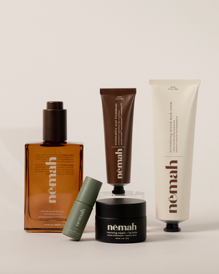 Five skincare products from nēmah including stretch mark therapy nourishing body oil, relaxing natural aromatherapy roll-on, restorative scar treatment, renewing nipple + lip balm, and revitalizing stretch mark cream, with visible product names and descriptions.