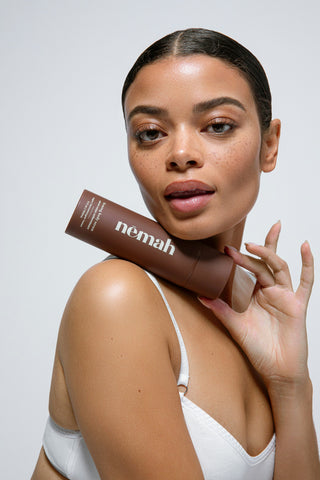 Model holding a brown bottle labeled 'nēmah firming body serum' on her shoulder