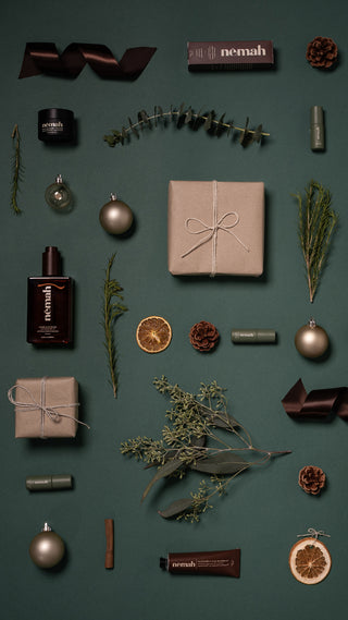 Festive flat-lay of Nemah skincare products and wrapped gifts on green background; labels read nemah restorative wax treatment