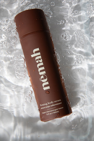 Brown bottle labeled 'nemah' firming body serum, vegan, dermatologist tested, 5 fl oz | 150 mL, submerged in water with bubbles