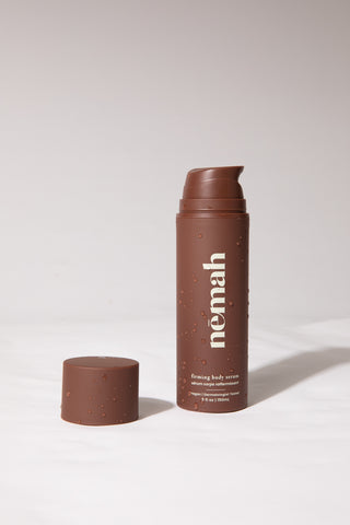 Brown bottle of Némain firming body serum with cap off, showing water droplets on surface