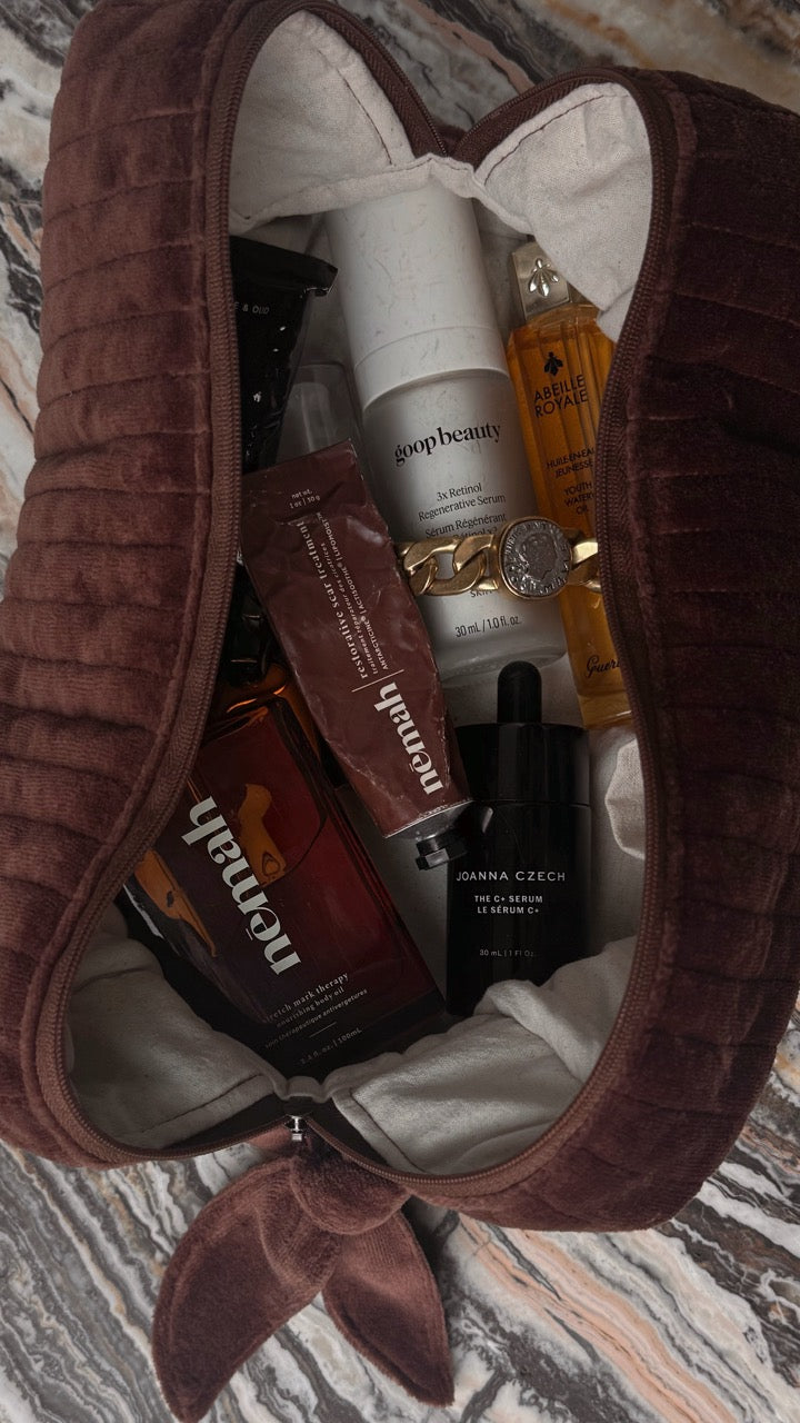 Brown velvet bag with skincare products inside, including serums and creams.