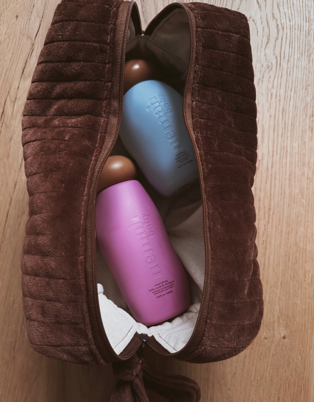 Two bottles inside a brown plush Beauty Bag on a wooden surface.