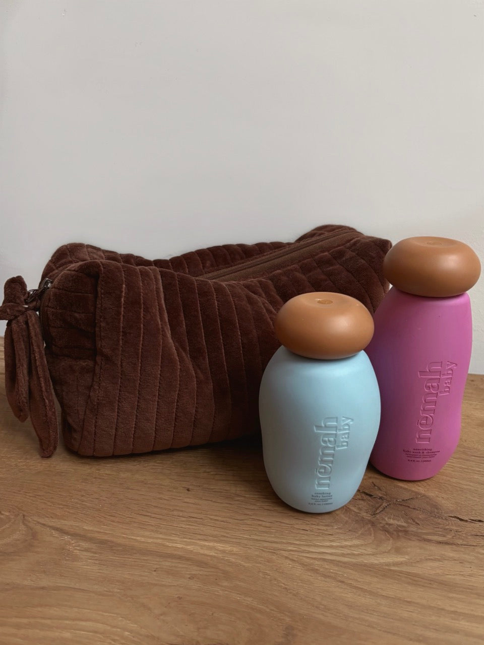 Two bottles next to a brown plush Beauty Bag on a wooden surface.