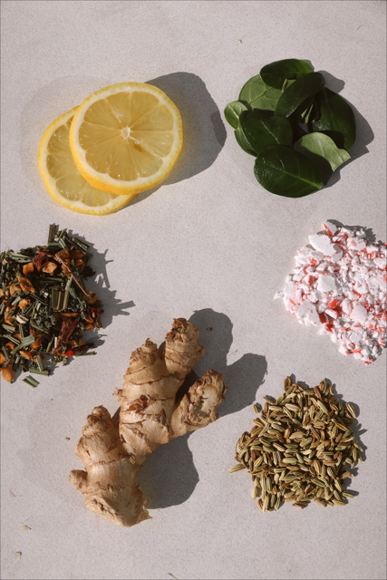 Ingredients including lemon slices, ginger, spices, and leaves on a surface.