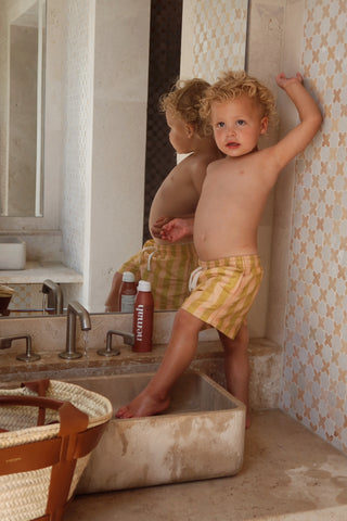 Toddler standing in sink beside bottle labeled 'nemah' on a bathroom counter