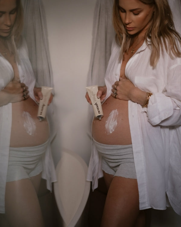 Pregnant woman applying cream to her belly in front of a mirror