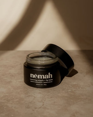 Open jar of nēmah renewing nipple + lip balm with black lid on a beige surface