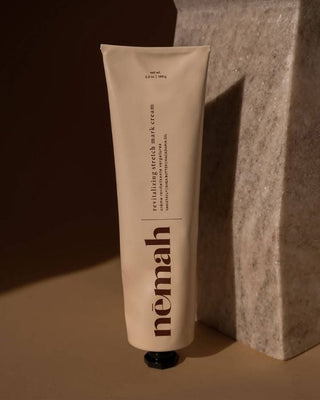 Tube of némah revitalizing stretch mark cream, 3.5 oz / 100 g, leaning against a marble slab